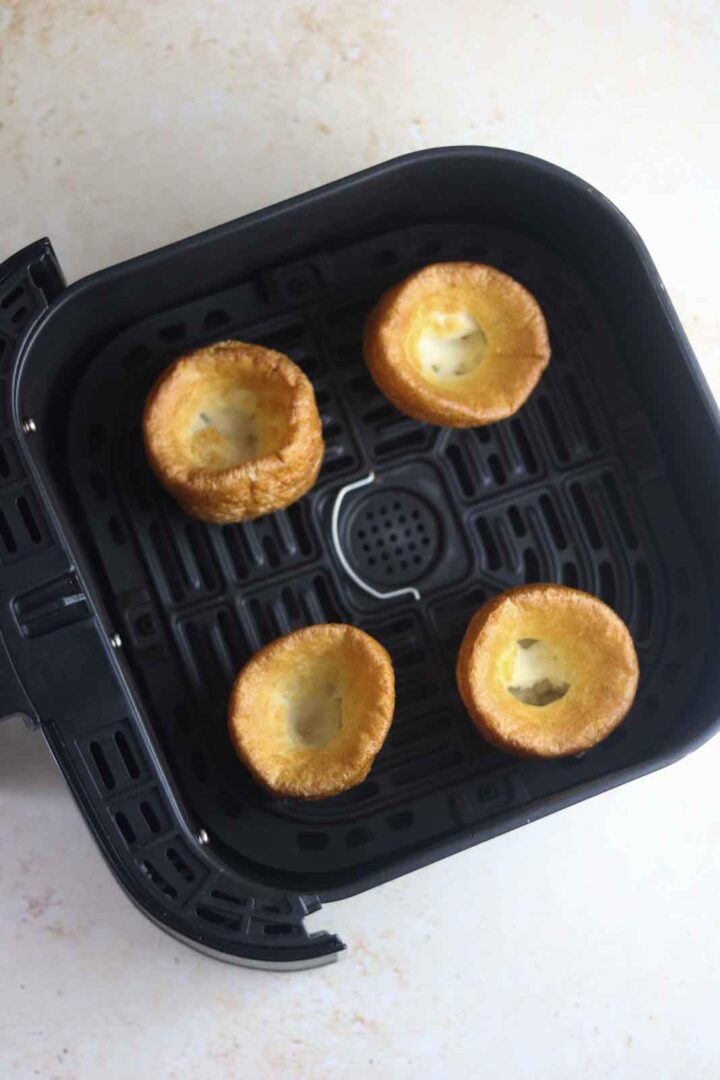 four golden-brown Yorkshire puddings in an air fryer basket.